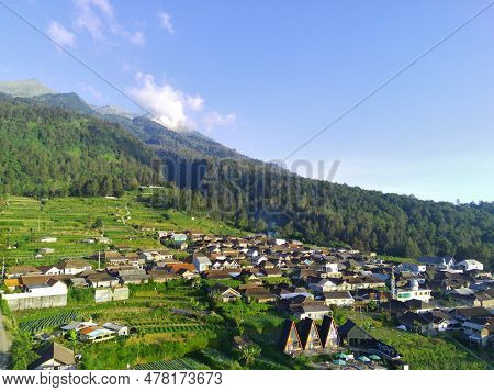 View Of Merbabu Mountain In Indonesia During Hazy Sunset With Green Village Foreground.