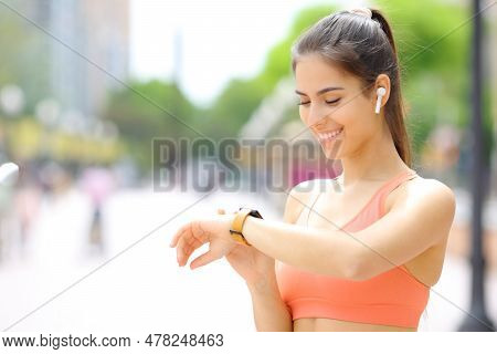 Happy Runner Wearing Earbud Selecting Music On Smartwatch Before Run In The Street