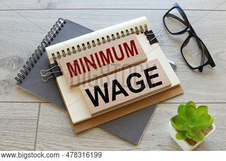 Minimum Wage At Blackboard Behind Stacked Coins. Text On Wooden Blocks