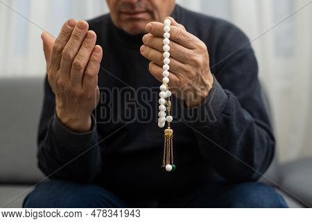 An Elderly Man Prays With A Rosary And The Flag Of The United Arab Emirates