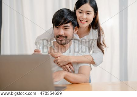 Happy Young Loving Family Couple Looking At Laptop Computer Screen, Reading Ecipes. Wife Showing Emb