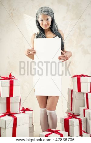 Belle jeune femme comme ange avec des tas de coffrets cadeaux maintenant vide tableau blanc