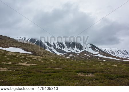Dramatic Alpine Landscape With Snowy Mountains In Gray Low Clouds. Bleak Atmospheric Scenery Of Tund