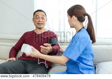 Caregiver Nurse Measuring Blood Pressure By Using Digital Sphygmomanometer Senior Patient At Home. C