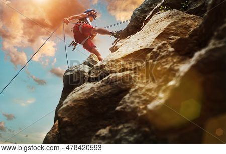 Muscular Climber Man In Protective Helmet Abseiling From Cliff Rock Wall Using Rope Belay Device And