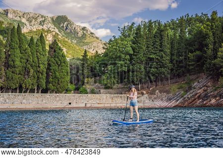Young Women Having Fun Stand Up Paddling In Blue Water Sea Near St Stefan Island Against The Backdro