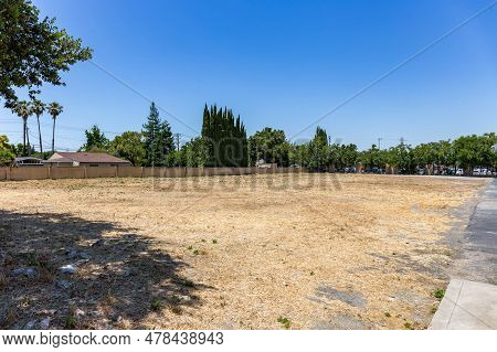 Photo Of A Vacant Field With Dead Grass And Trees And A Blue Sky