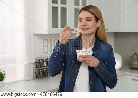 Woman Eating Tasty Yogurt With Spoon In Kitchen. Space For Text