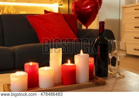 Romantic Atmosphere. Burning Candles, Bottle Of Wine And Glasses On Wooden Table Near Sofa In Room D