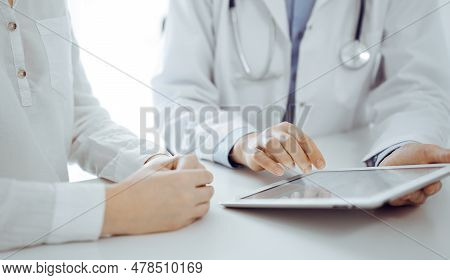 Doctor And Patient Sitting Near Each Other At The Desk In Clinic. The Focus Is On Female Physicians 