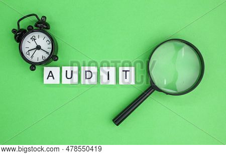 Magnifying Glass And Alarm Clock With The Word Audit. Audit Concept. The Concept Of Assessing Someth