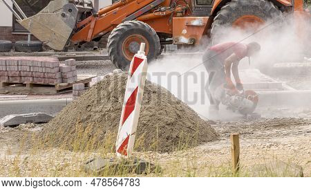 Road Building . Paving Stone Cutting. Worker In A White Cloud Of Concrete Dust With A Petrol Saw (an