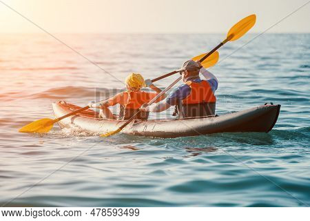 Happy Couple Kayaks In An Inflatable Kayak On The Sea At Sunset. Couple Kanoeing In The Sea Near The