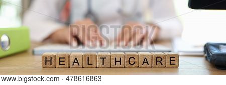 Close-up Of Healthcare Word Collected With Wooden Cubes In Row. Woman Doctor In Medical Gown On Back