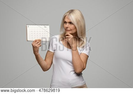 Menopause Concept. Pensive Mature Woman Looking At Blank Menstrual Calendar