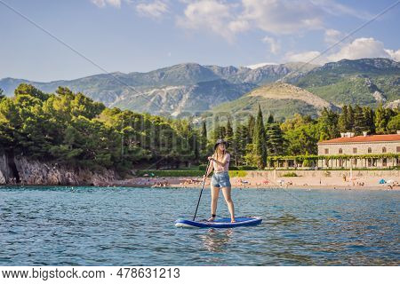 Young Women Having Fun Stand Up Paddling In Blue Water Sea Near St Stefan Island Against The Backdro