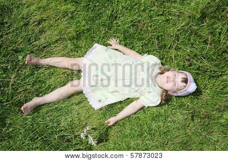 Little Barefoot Girl Lies On Green Grass Of Meadow At Summer Sunny Day