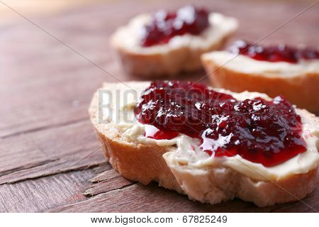 Fresh bread with homemade butter and blackcurrant jam on wooden background