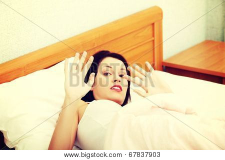 Sceared woman is lying in bed and protect by hands, in home. Violence concept.