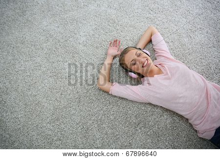 Blond girl relaxing on carpet floor with headphones on