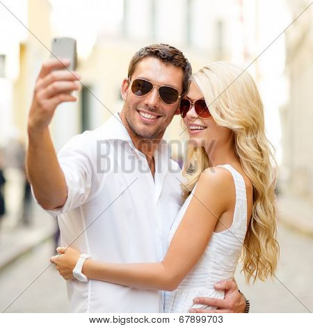 summer holidays, technology, love, relationship and dating concept - smiling couple taking selfie with smartphone in the city