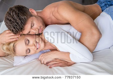 Close up Romantic Young Couple Lying on White Bed with Handsome Topless Guy Embracing her Beautiful Smiling Partner in Long Sleeve Shirt.