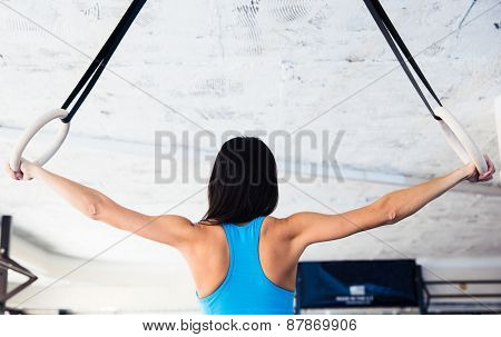 Back view portrait of woman working out on gimnastic rings at gym