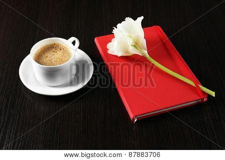 Cup of coffee with notebook and fresh flower on wooden table background