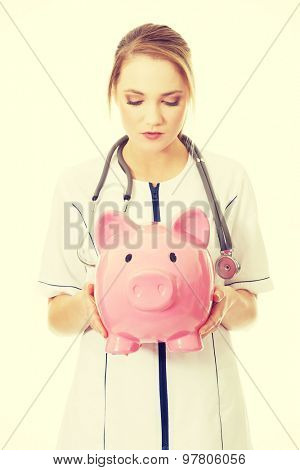 Young beautiful female doctor holding a piggybank.