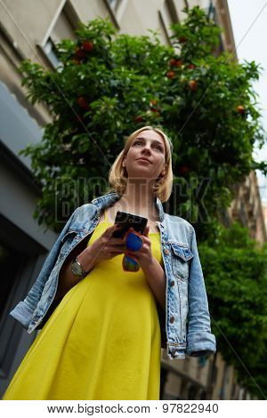 Low angle view with young female tourist using telephone for navigation while standing outdoors