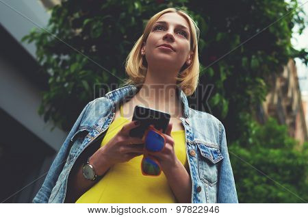 Low angle view with pretty young woman hold smartphone standing on mandarin tree background in city