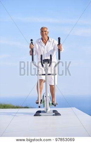 healthy senior man working out on gym treadmill machine at modern home terace with ocean view