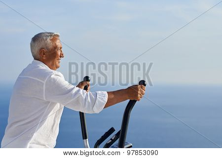 healthy senior man working out on gym treadmill machine at modern home terace with ocean view