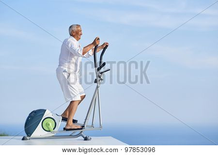 healthy senior man working out on gym treadmill machine at modern home terace with ocean view