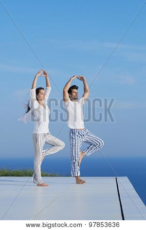 young couple practicing yoga at sunset in modern home terace with ocean and sunset in background