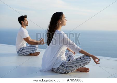 young couple practicing yoga at sunset in modern home terace with ocean and sunset in background