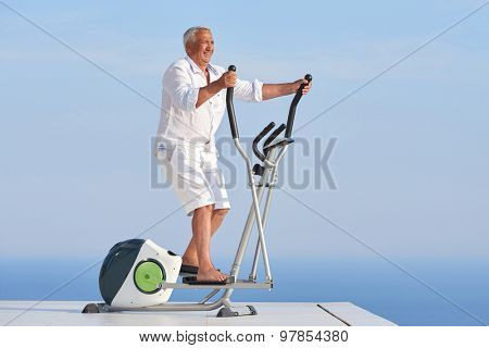 healthy senior man working out on gym treadmill machine at modern home terace with ocean view