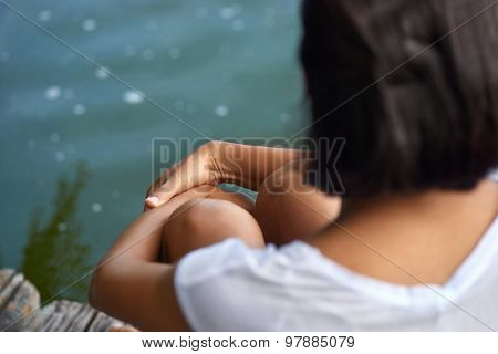 Rear view of young female sitting near a lake or pond on a wooden jetty
