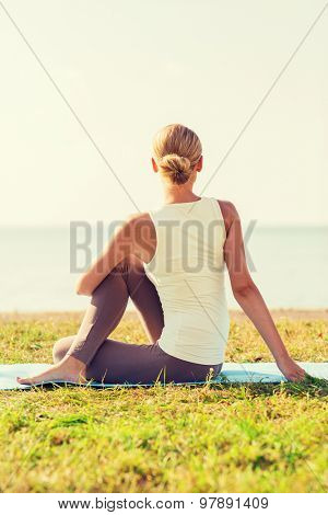 fitness, sport, people and lifestyle concept - woman making yoga exercises on mat outdoors from back