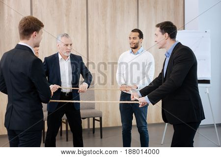 Team building activity. Nice pleasant delighted people standing in a circle and holding a rope while doing a teambuilding activity