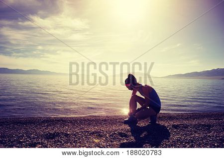 Healthy young fitness woman trail runner tying shoelace on seaside