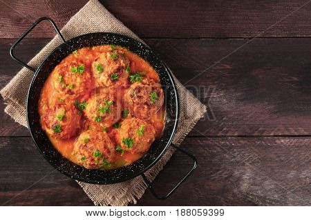 An overhead photo of meatballs in tomato sauce, shot from above in the skillet on dark rustic textures, with a place for text