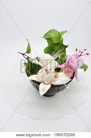 a few really nice flowers of fuchsia and black glass small Cup on a white Lacy napkin