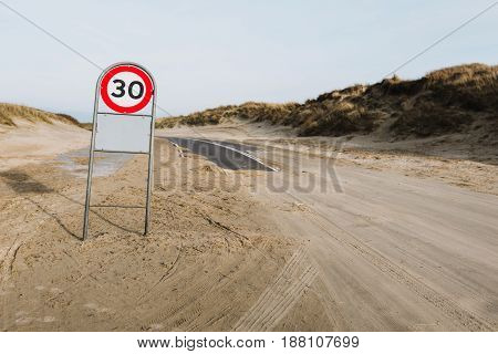 Asphalt road covered with sand and 30km/h sign