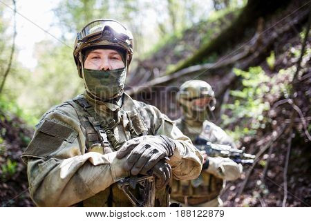 Military men in helmet and camouflage with gun on forest background