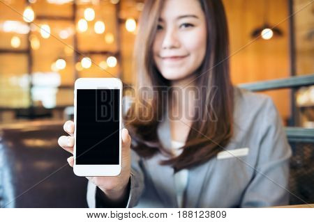 Mockup image of an Asian beautiful business woman holding and showing white mobile phone with blank black screen in cafe