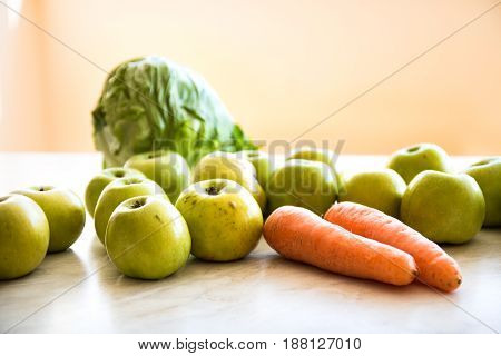 Two orange carrots green apples bunch of dill and head of cabbage on the table. Close-up view. Orange background