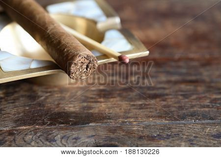 One Cuban cigar near matchstick on old wooden background