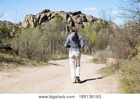 Woman Hiker Is Walking To The Rocks. White Road, Bushes And Trees, Springtime
