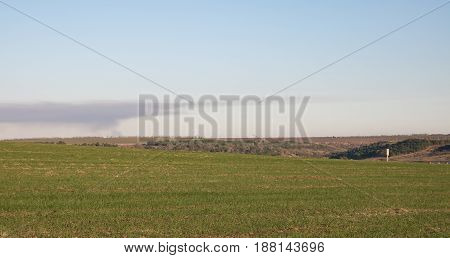 green field, smoke on the horizon, water pump house in the right corner, blue sky, sunset